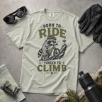 Bay green t-shirt with a graphic of a raccoon riding a bike and text 'Born to Ride, Forced to Climb'.