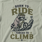 Bay green t-shirt with a graphic of a raccoon riding a bike and text 'Born to Ride, Forced to Climb'.