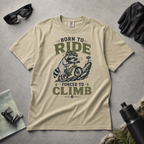 Khaki colored t-shirt with a graphic of a raccoon riding a bike and text 'Born to Ride, Forced to Climb'.