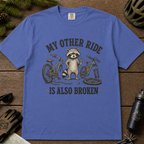 Mystic blue t-shirt with a raccoon and bicycle graphic on a wooden surface.