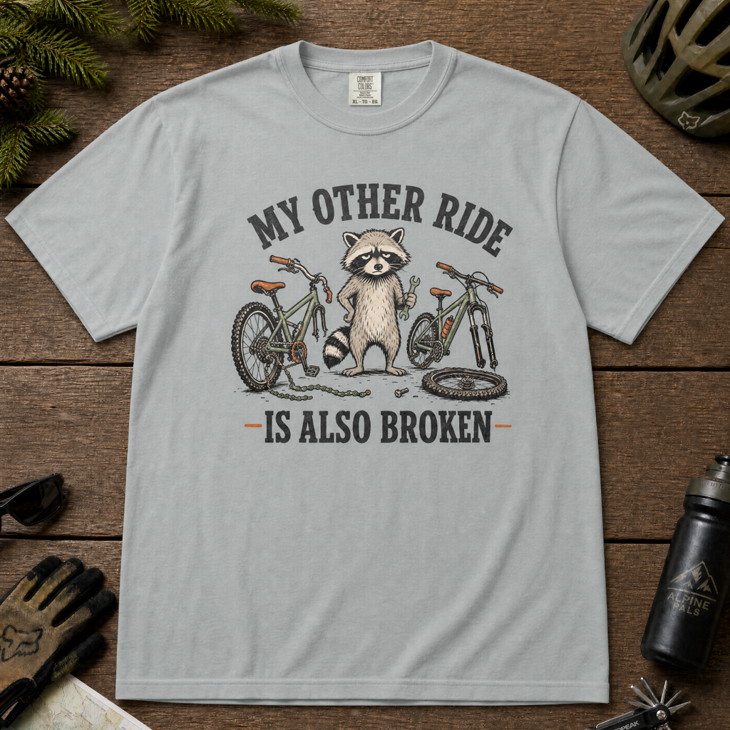 Granite gray t-shirt with a raccoon graphic and text on a wooden surface with outdoor gear.