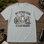 Granite gray t-shirt with a raccoon graphic and text on a wooden surface with outdoor gear.