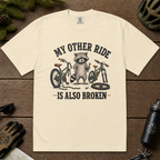 Ivory white t-shirt with raccoon graphic and text on a wooden surface with cycling accessories.