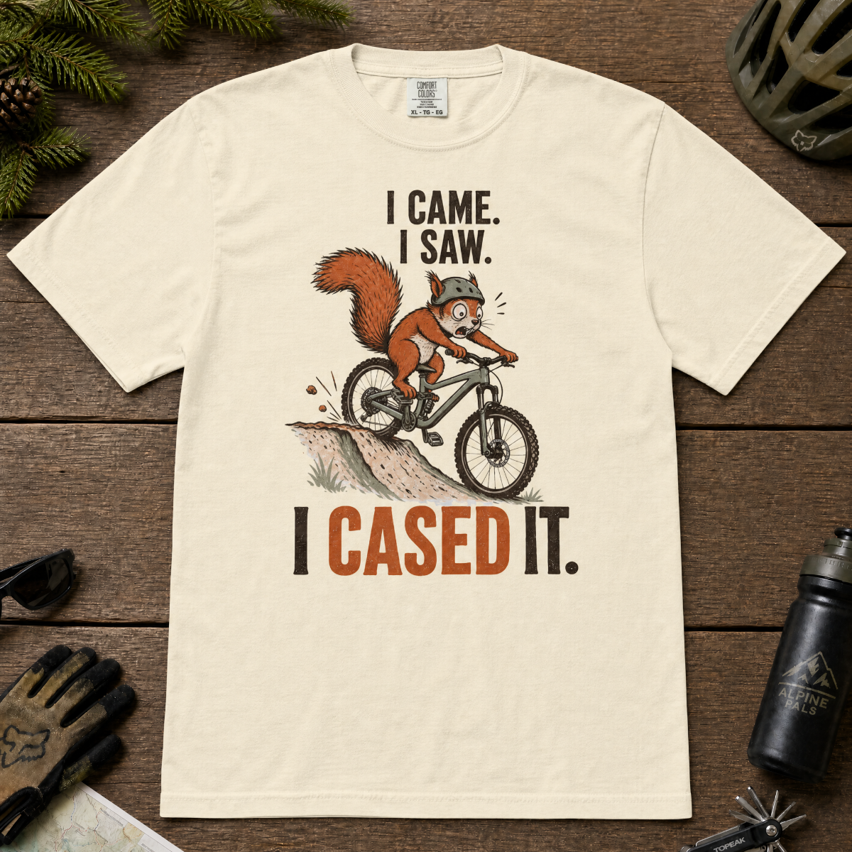 Ivory white t-shirt with a graphic of a squirrel on a bike and text 'I Came. I Saw. I Cased It.' on a wooden surface.