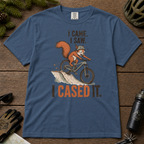 Midnight blue t-shirt with a graphic of a squirrel on a bike and text 'I came. I saw. I cased it.' on a wooden surface.