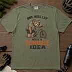 Moss green t-shirt with bear graphic and text on a wooden surface with outdoor gear.