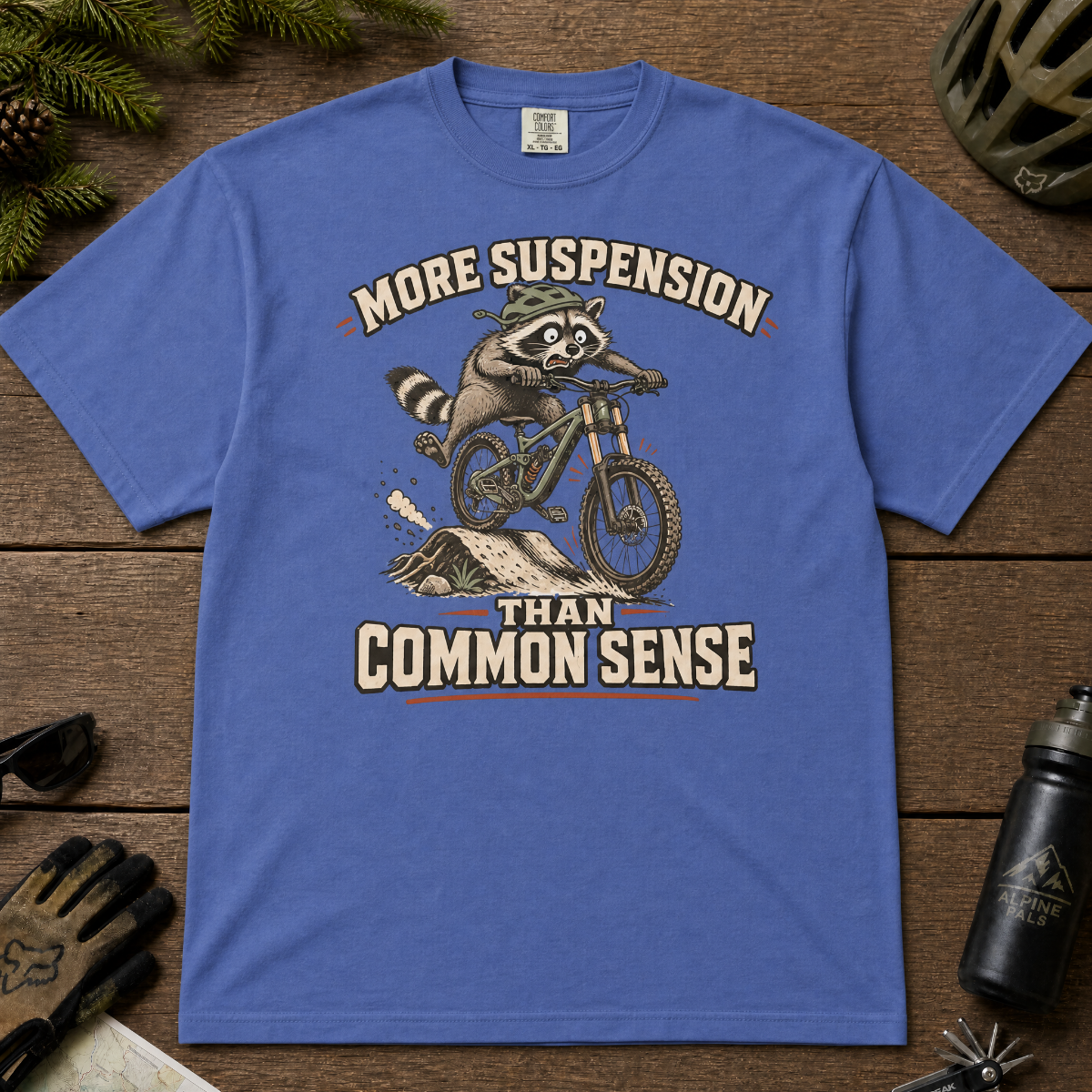 Mystic blue t-shirt with a raccoon riding a bike graphic and text 'More suspension than common sense'.