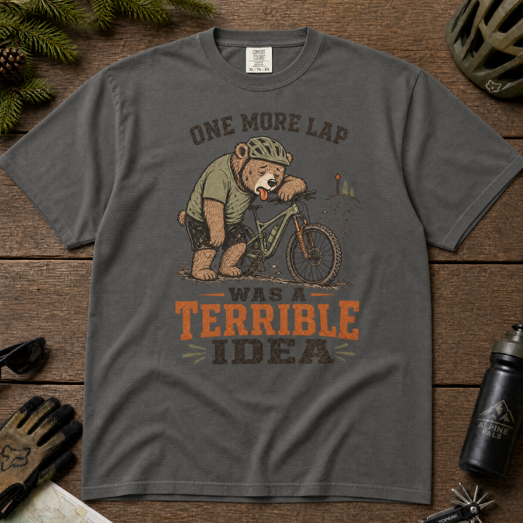 Pepper gray t-shirt with bear graphic and text on a wooden surface with cycling accessories.
