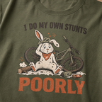 Hemp green t-shirt with a graphic of a rabbit and bicycle and text 'I do my own stunts poorly' on a plain background.