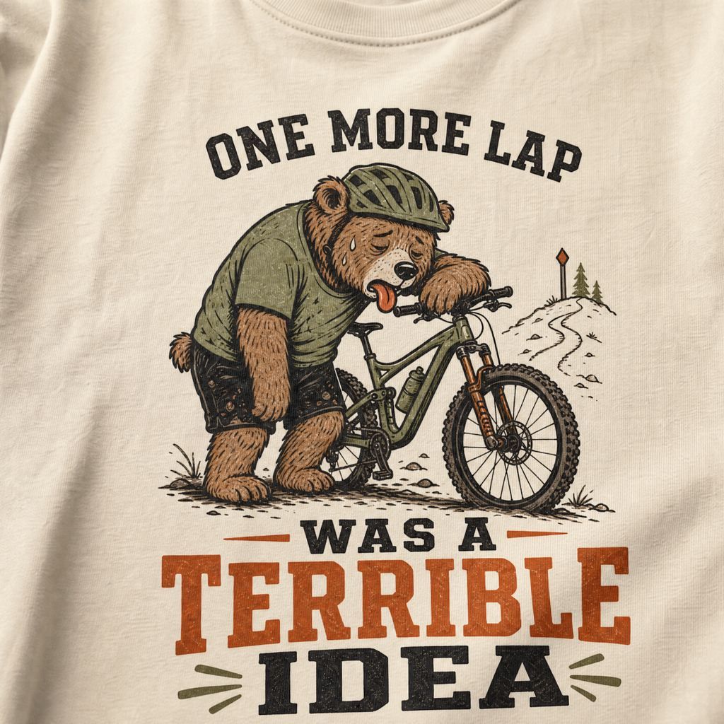 T-shirt with a bear riding a bike and text 'One more lap was a terrible idea' on a ivory white background