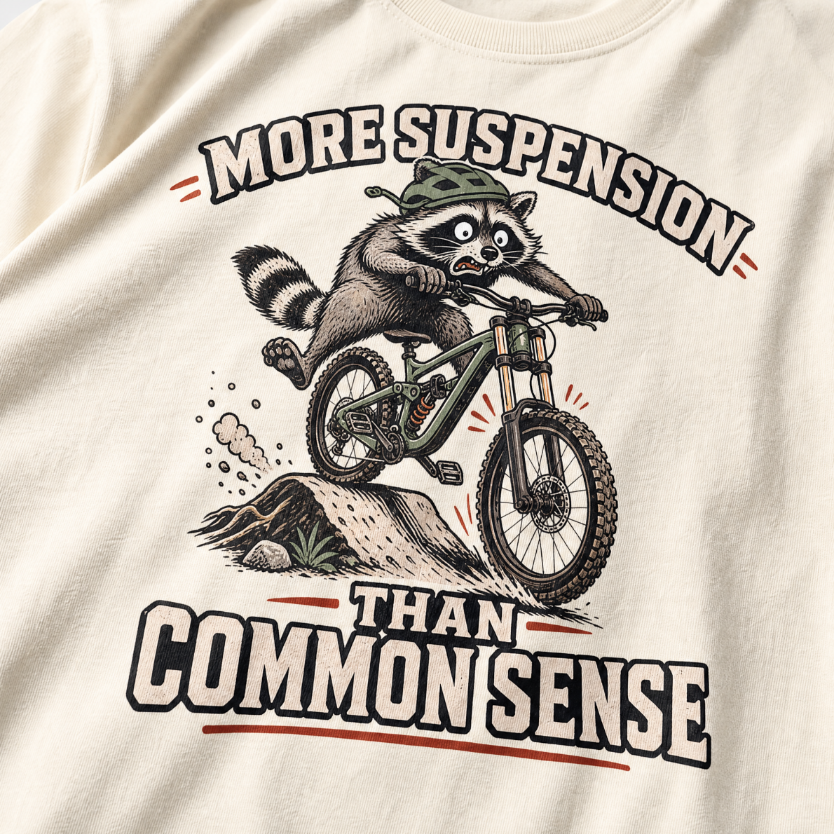 Ivory white t-shirt with a raccoon riding a bike graphic and text 'More suspension than common sense'.
