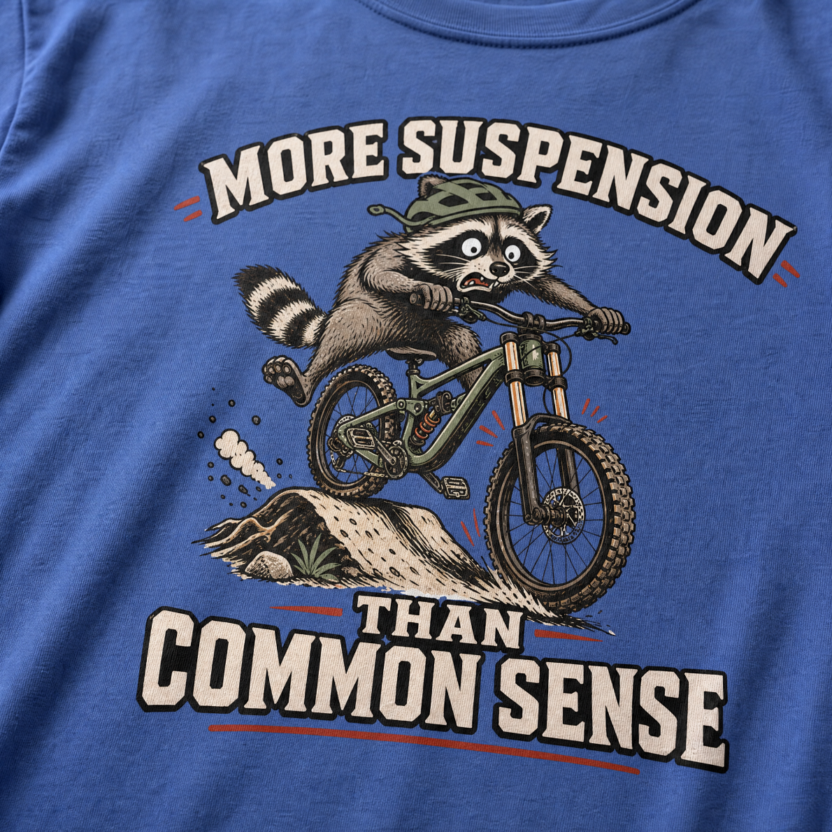 Mystic blue t-shirt with a raccoon riding a bike graphic and text 'More suspension than common sense'.
