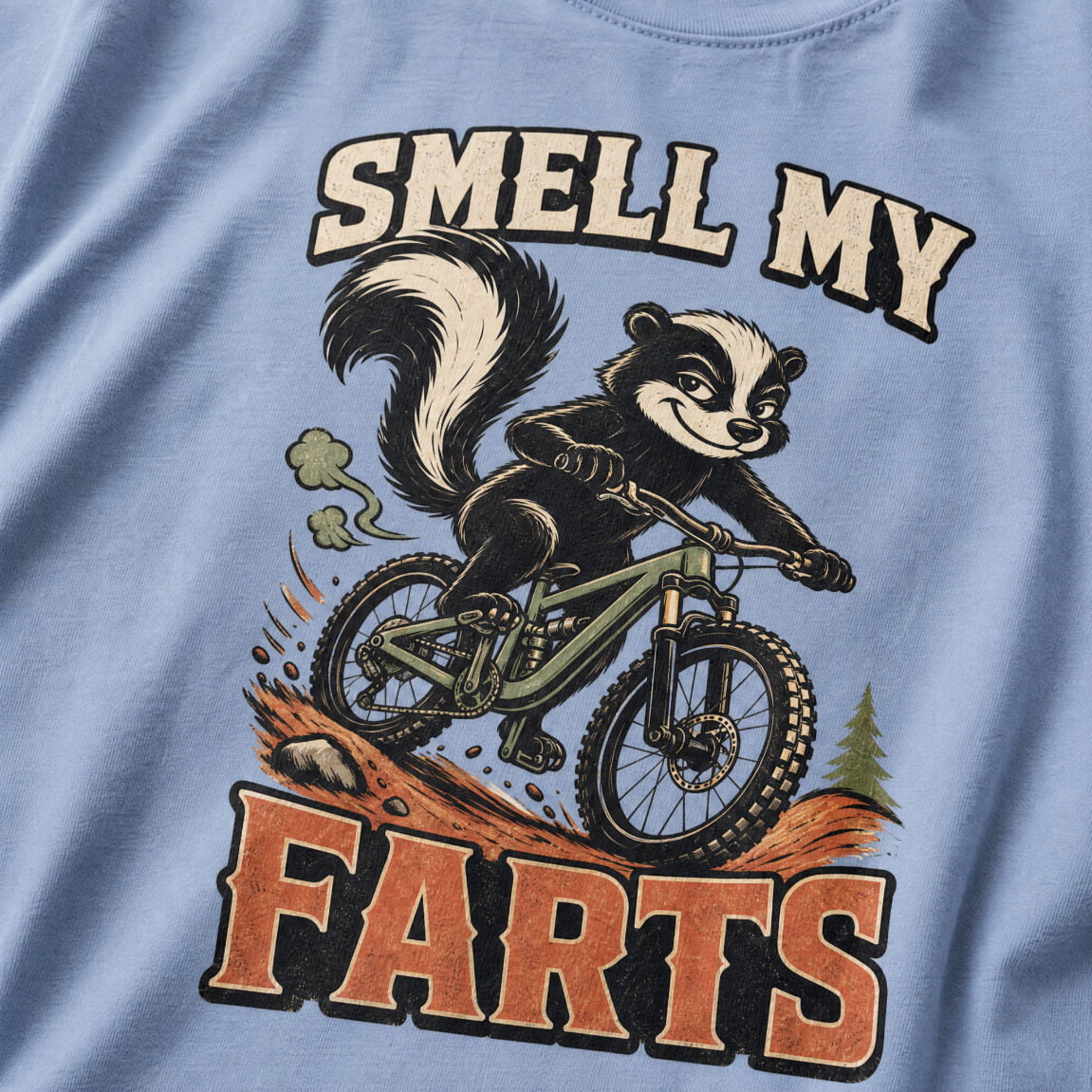 Washed denim blue t-shirt with a graphic of a raccoon on a bike and text 'SMELL MY FARTS'.