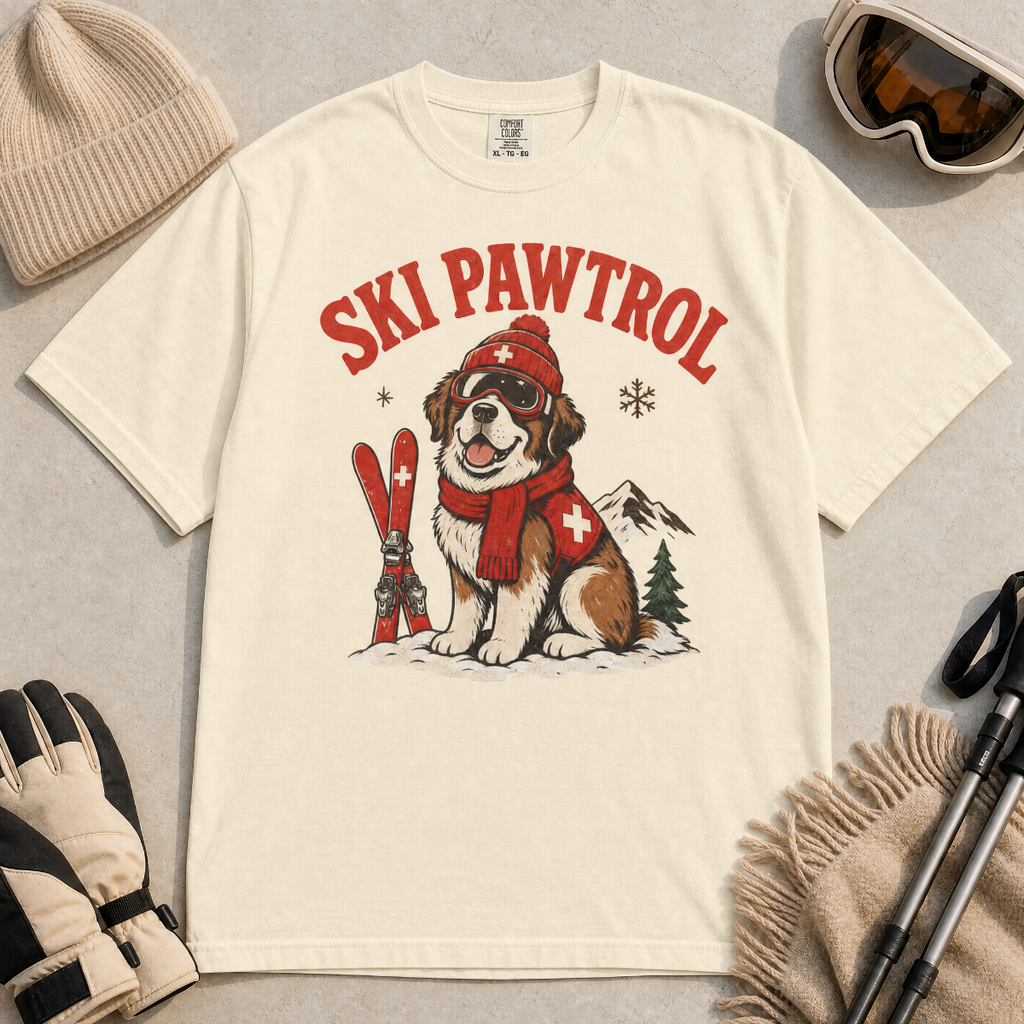 Ivory white t-shirt with a dog graphic and 'Ski Pawtrol' text, surrounded by winter accessories on a light background.