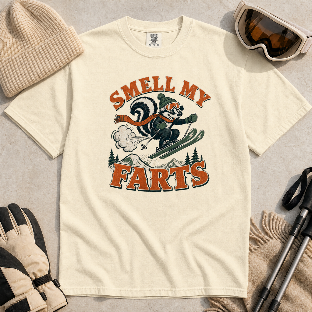 Ivory white t-shirt with a graphic design featuring a skier and text 'Smell My Farts' on a textured surface.