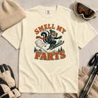 Ivory white t-shirt with a graphic design featuring a skier and text 'Smell My Farts' on a textured surface.