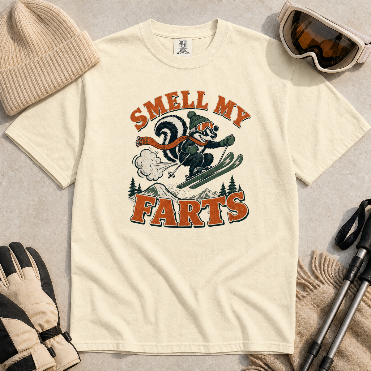 Ivory white t-shirt with a graphic design featuring a skier and text 'Smell My Farts' on a textured surface.