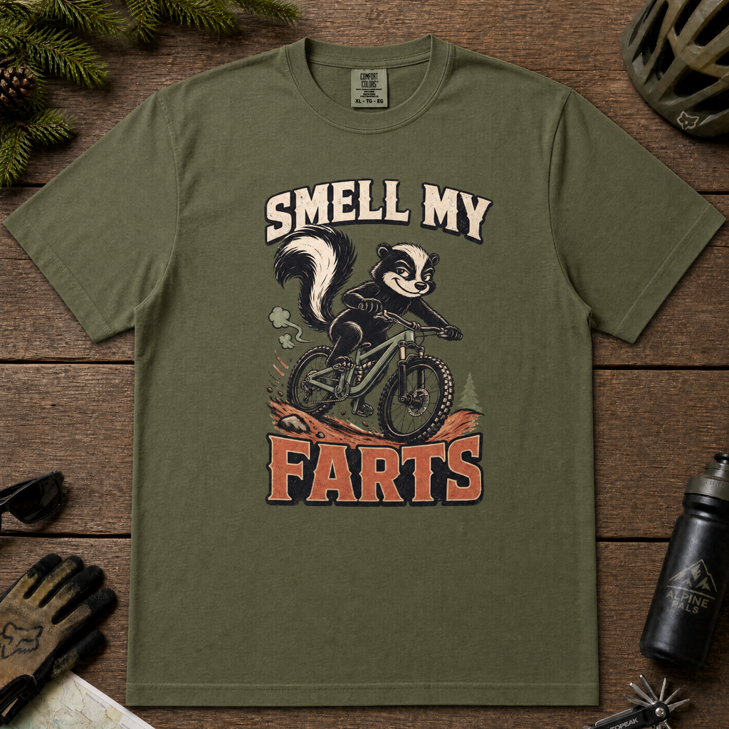 Hemp green t-shirt with a graphic of a skunk on a bike and text 'Smell My Farts' on a wooden surface.