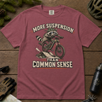 Brick red t-shirt with a raccoon riding a bike graphic and text 'More suspension than common sense'.
