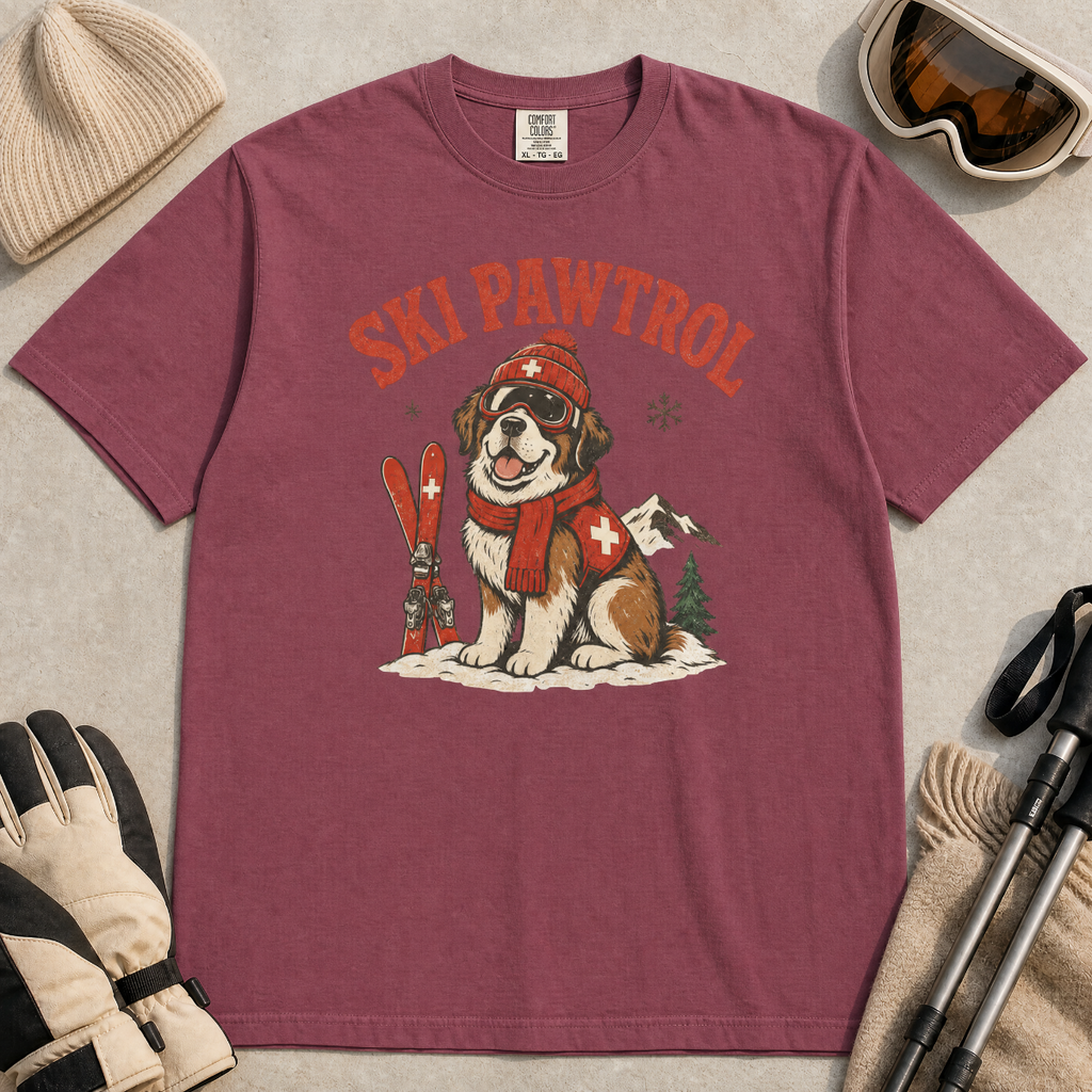 Brick red t-shirt with a dog graphic and 'Ski Pawtrol' text, surrounded by winter accessories on a light background.