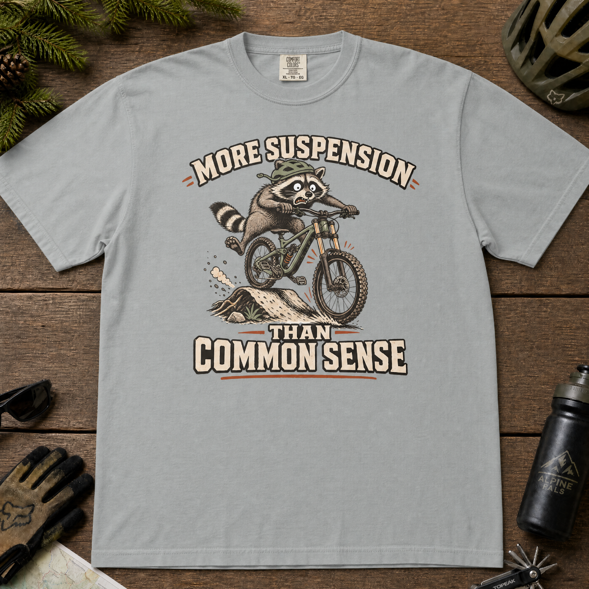Granite gray t-shirt with a raccoon riding a bike graphic and text 'More suspension than common sense'.