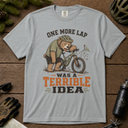 Granite gray t-shirt with bear on bike graphic and text on wooden surface with outdoor gear.