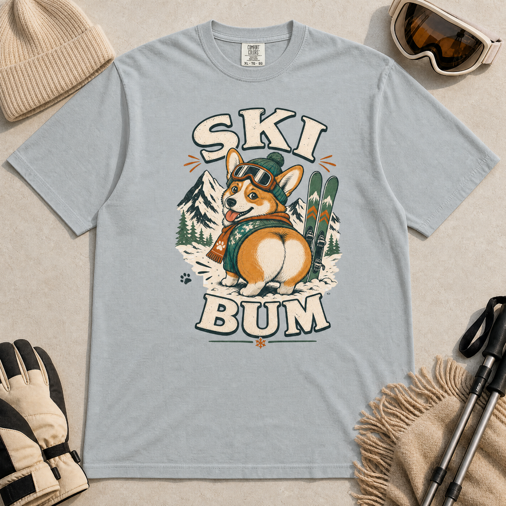 Granite gray t-shirt with a corgi graphic and 'Ski Bum' text, surrounded by skiing accessories on a beige background.