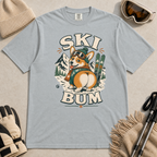 Granite gray t-shirt with a corgi graphic and 'Ski Bum' text, surrounded by skiing accessories on a beige background.