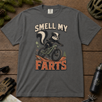 Pepper gray t-shirt with a graphic of a skunk on a bike and text 'SMELL MY FARTS' on a wooden surface.