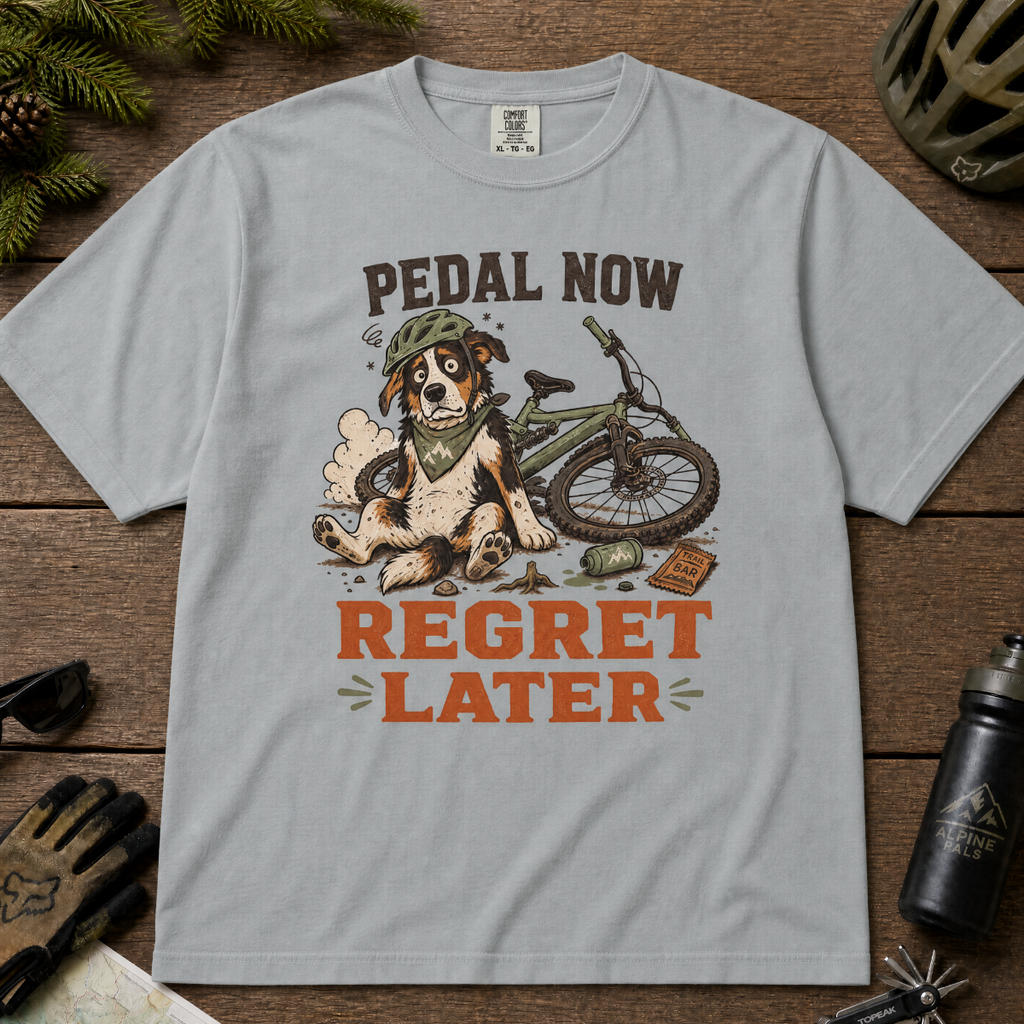 Granite gray t-shirt with a graphic of a dog with a bicycle and text 'Pedal Now Regret Later' on a wooden surface.