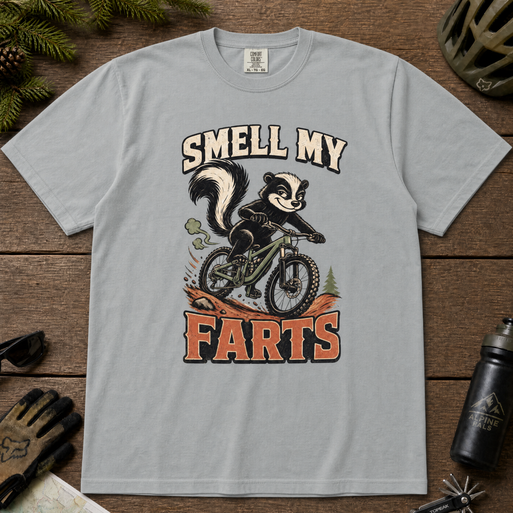 Granite gray t-shirt with a graphic of a skunk on a bike and text 'Smell My Farts' on a wooden surface.