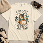 Ivory white t-shirt with a corgi graphic and 'Ski Bum' text, surrounded by winter accessories on a gray surface.