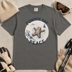 Flat lay of a pepper gray t-shirt featuring a peaceful bear snow angel ski graphic with “Powder Day Peace” text, styled with winter accessories.