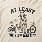 Ivory white t-shirt of a goat holding a bicycle pedal with a broken mountain bike surrounding it. Included text, "At Least the View Was Nice".