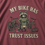 Brick red t-shirt with a raccoon graphic and text 'My bike has trust issues' on a plain background