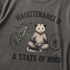 Pepper gray t-shirt featuring a possum meditating while fixing a bike with text, "Maintenance is a State of Mind".