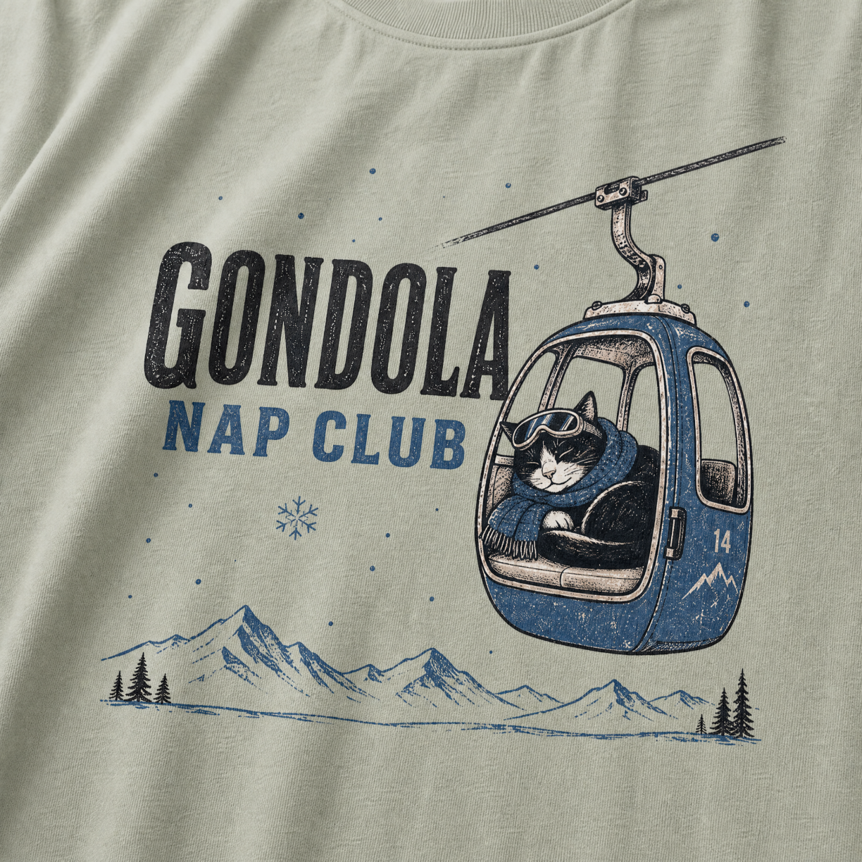 Bay green t-shirt featuring a cat napping in a ski gondola with text, "Gondola Nap Club".