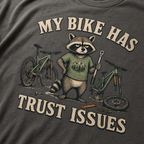 T-shirt with a raccoon graphic and bicycle-themed text on a pepper gray background