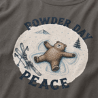 Close-up of a pepper gray t-shirt with a vintage ski design showing a relaxed bear making a snow angel beside skis, with “Powder Day Peace” text.