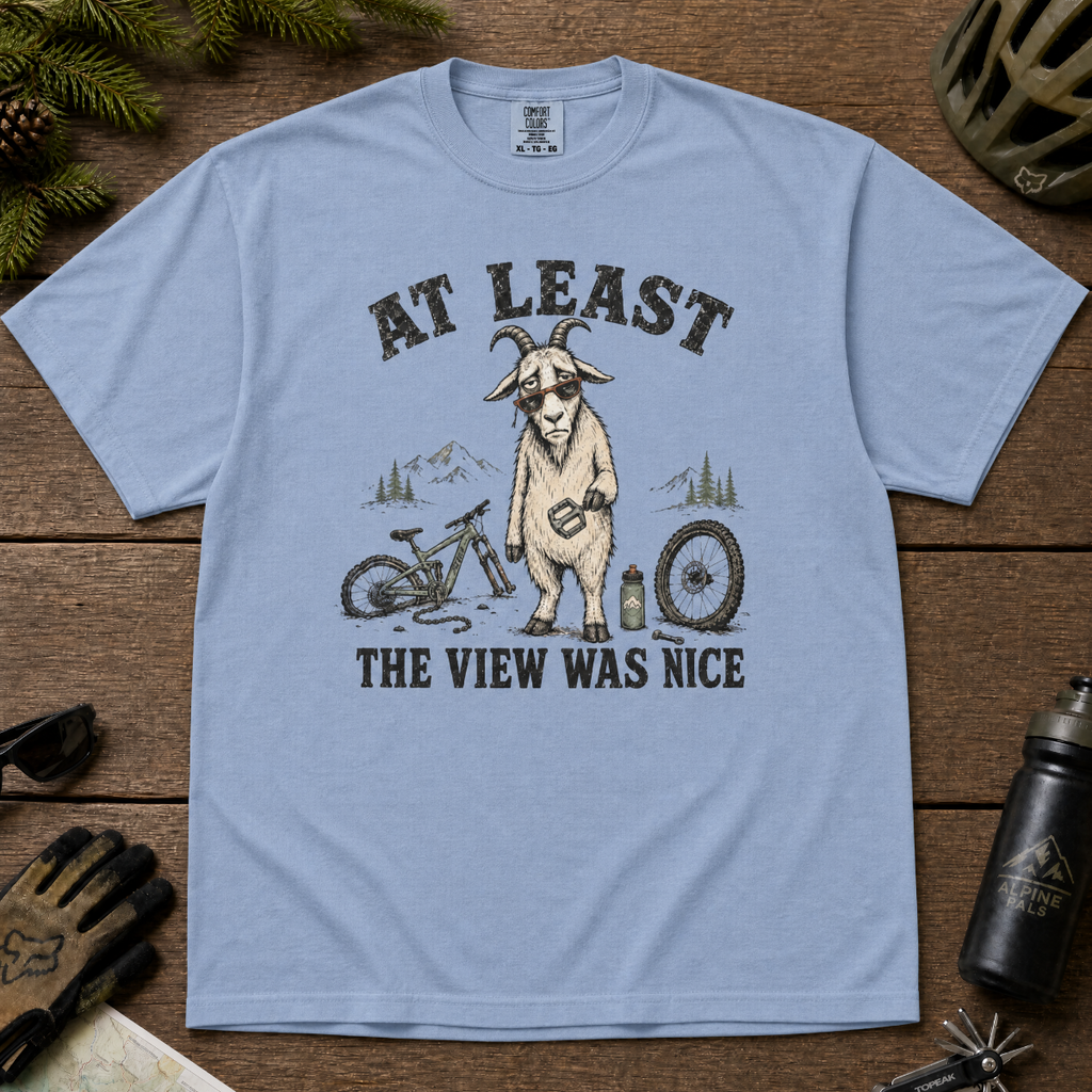 Washed denim blue t-shirt of a goat holding a bicycle pedal with a broken mountain bike surrounding it. Included text, "At Least the View Was Nice".