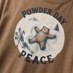 Close-up of an espresso brown t-shirt with a vintage ski design showing a relaxed bear making a snow angel beside skis, with “Powder Day Peace” text.