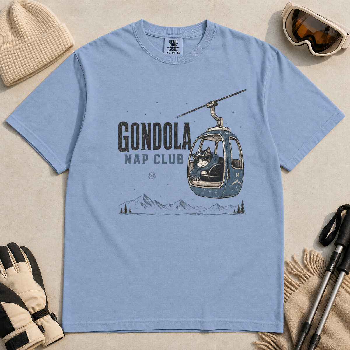 Washed denim blue t-shirt featuring a cat napping in a ski gondola with text, "Gondola Nap Club".
