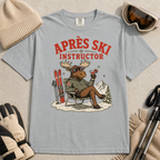 Granite gray t-shirt with a moose graphic and 'Après Ski Instructor' text, surrounded by skiing accessories on a beige background.