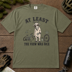 Moss green t-shirt of a goat holding a bicycle pedal with a broken mountain bike surrounding it. Included text, "At Least the View Was Nice".