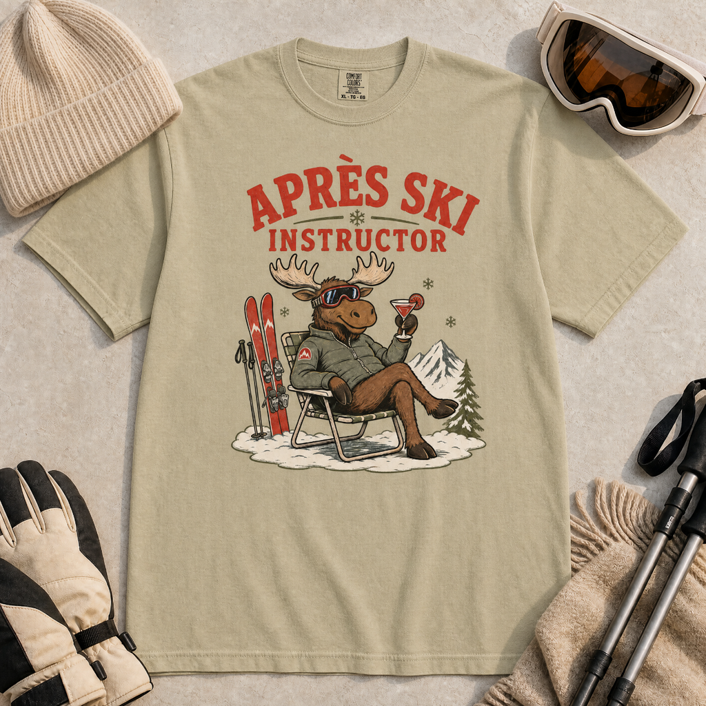 Khaki colored t-shirt with 'Après Ski Instructor' graphic, surrounded by skiing accessories on a beige background.