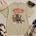 Khaki colored t-shirt with 'Après Ski Instructor' graphic, surrounded by skiing accessories on a beige background.