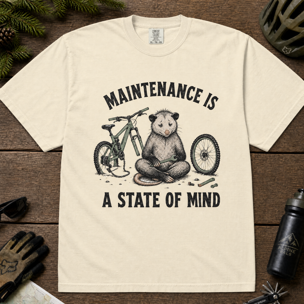 Ivory white t-shirt featuring a possum meditating while fixing a bike with text, "Maintenance is a State of Mind".