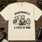 Ivory white t-shirt featuring a possum meditating while fixing a bike with text, "Maintenance is a State of Mind".
