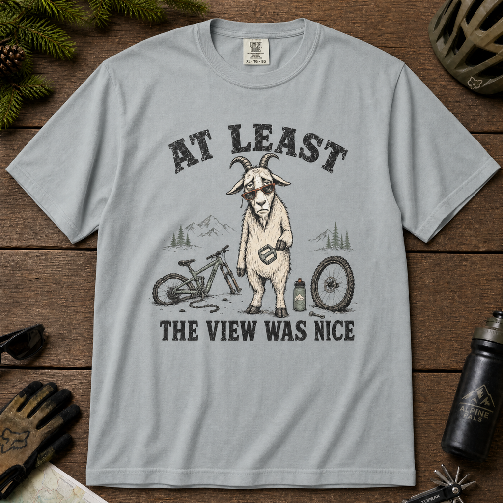 Granite gray t-shirt of a goat holding a bicycle pedal with a broken mountain bike surrounding it. Included text, "At Least the View Was Nice".