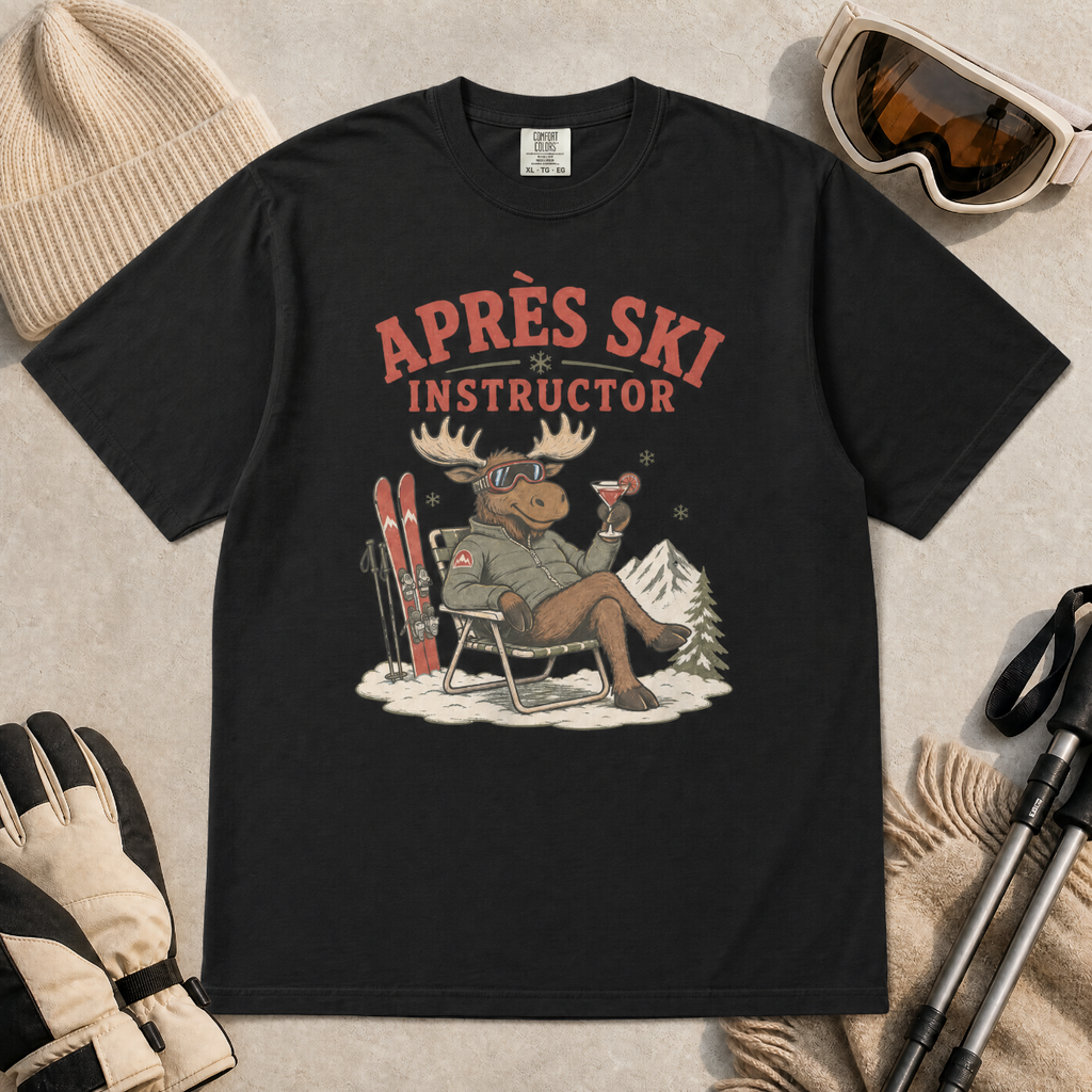 Black t-shirt with 'Après Ski Instructor' design featuring a moose, surrounded by skiing accessories on a beige background.